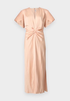 Woman with dark hair wearing a peach-colored midi dress with puff sleeves and ruched waist, paired with black lace-up heels, standing against white background.