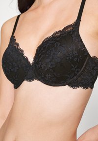 Black lace bra with a floral pattern, padded cups, scalloped edges, and adjustable straps, showcasing a lightweight, textured design.