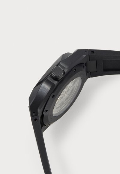 Black wristwatch with an octagonal case, textured finish, a visible movement through a transparent back, and a hexagonal crown.