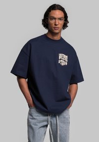 Marineblauw oversized t-shirt van katoen, met een witte grafische print op de linkerborst, gecombineerd met lichtblauwe spijkerbroek.