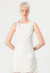 Vestido sin mangas blanco con un patrón de cuadros, que presenta un detalle de hombro retorcido, tejido texturizado y silueta ajustada.