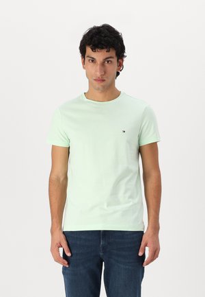 Helles mintgrünes Baumwoll-T-Shirt mit Rundhalsausschnitt, kurzen Ärmeln und einem kleinen Logoschriftzug auf der Brust. Getragen mit dunkelblauen Jeans.