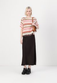Häkeloberteil mit roten, pinken und beigen Streifen, mit einem Fransensaum. Schwarze Satinmaxi-Rock und klobige schwarze Plateau-Schuhe.