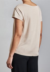 Beige kortärmad skjorta med rundad halsringning, mjuk textur, enkel design och synlig sömdetalj på baksidan. Matchad med svarta byxor.