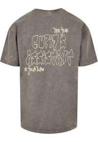 Grå oversized t-shirt lavet af bomuld med en falmet tekstur. Har et stiliseret hvidt tryk på ryggen: "I år er Københavns Assistent din tur."