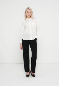 Camisa blanca abotonada con un solo bolsillo en el pecho, combinada con pantalones negros de pierna recta y tacones negros de punta puntiaguda. Líneas limpias y tela ligera.