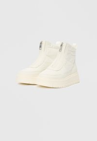 Et par off-white høye støvler med tykke såler, frontglidelåser og subtilt sydd stjernemønster på sidene mot en ensfarget bakgrunn.