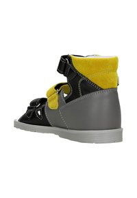 Scarpa nera e grigia con accenti gialli; realizzata in camoscio e pelle. Presenta cinturini a strappo e dettagli ritagliati.