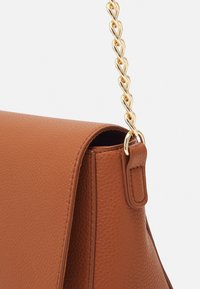 Brązowa skórzana torebka o teksturalnym wykończeniu, z złotym łańcuszkiem na ramię i usztywnioną konstrukcją. Zauważalne detale to ściegi na brzegach.