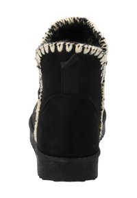 Botte en daim noire avec une doublure en laine crème texturée, surpiqûres contrastantes autour de la cheville, et une languette de traction à l'arrière. Semelle en caoutchouc plate.