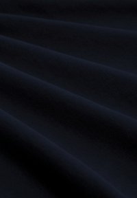 Donker marineblauwe stof met zachte plooien die diagonale schaduwen enHighlights creëren, wat textuur en diepte laat zien.