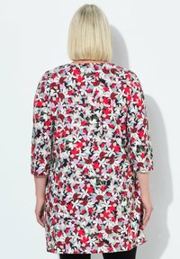 Bloemrijke tuniek met driekwart mouwen, voorzien van een levendig patroon in rood, roze, wit en groen op een lichte achtergrond.