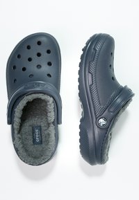 Des Crocs bleu marine avec une douce doublure en polaire grise, dotés de trous de ventilation, d'une forme arrondie et de semelles en caoutchouc texturé pour une meilleure adhérence.