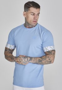 Světlomodré sportovní tričko s hladkým povrchem, kulatým výstřihem a bílými pruhovanými akcenty na rukávech s textem.