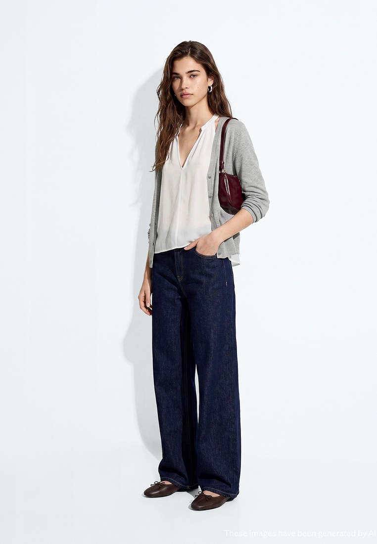 Femme portant un chemisier blanc, un cardigan gris, un jean large foncé, des ballerines marron et portant un petit sac à bandoulière bordeaux.