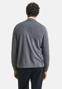 Grauer gestrickter Pullover mit rundem Halsausschnitt, gerippten Bündchen und Saum, der eine glatte Textur und eine figurbetonte Passform aufweist. Kombiniert mit dunklen Hosen.