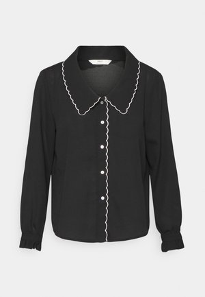 Blusa preta de mangas longas com colarinho serrilhado e acabamento branco, com botões na frente e punhos franzidos. Feita de tecido leve.