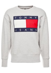 Sudadera gris con cuello redondo, que presenta un logotipo audaz en rojo, blanco y azul marino. El material parece suave con puños y dobladillo acanalados.