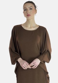 Robe pull marron surdimensionnée avec des manches larges, un décolleté bateau et des détails drapés, fabriquée dans un tissu léger et lisse.