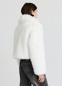 Weiße Jacke aus Kunstpelz, kurz geschnitten, mit weitem Kragen, weicher Textur und langen Ärmeln. Gestylt mit schwarzen, hoch taillierten Jeans.