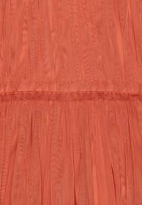 Zbliżenie na pomarańczową przezroczystą tkaninę z marszczeniem i plisowaniem, tworzącą poziome detale szwów.