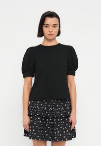 Μαύρο τοπ με υφή και κοντά φουσκωτά μανίκια, σε συνδυασμό με μια στρωματοποιημένη μπλε φλοράλ φούστα με μικρά, λεπτά σχέδια.