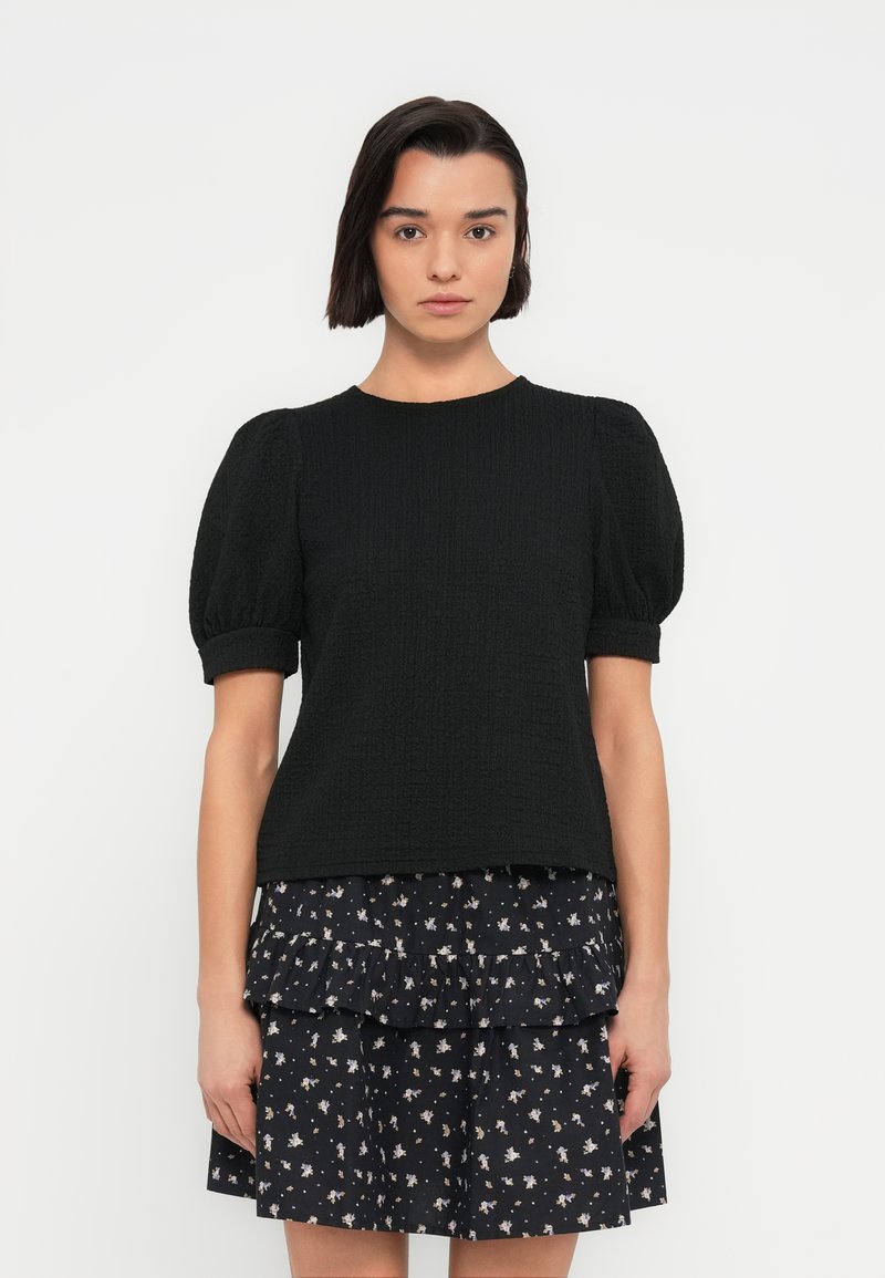 Μαύρο τοπ με υφή και κοντά φουσκωτά μανίκια, σε συνδυασμό με μια στρωματοποιημένη μπλε φλοράλ φούστα με μικρά, λεπτά σχέδια.