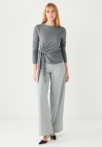 Gray long-sleeve top with a knotted detail at the waist paired with light gray wide-leg trousers and black pointed-toe heels.