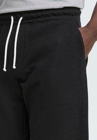 Pantalones de chándal negros con una cintura elástica, cordón blanco y bolsillos laterales. La tela tiene una textura suave y lisa.