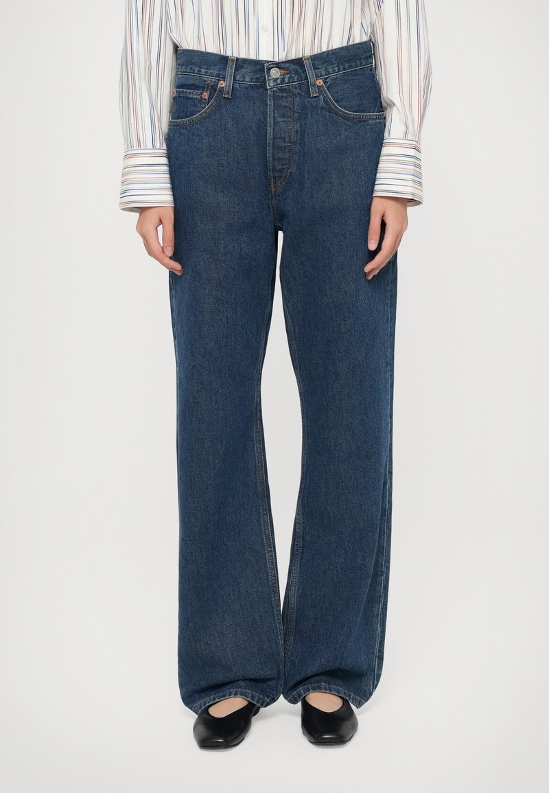 Wide-leg blue denim jeans with a high waist, featuring classic five-pocket design and copper-tone hardware. Smooth texture, straight legs.
