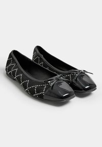 Bailarinas negras con una parte superior de ante que presenta patrones de diamantes blancos, punteras de charol brillantes y un lazo decorativo en la parte delantera.