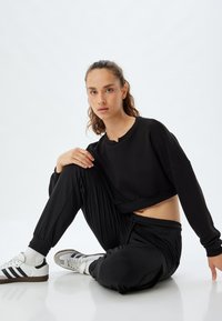 Zwarte cropped sweatshirt met ronde hals, gecombineerd met zwarte taper joggers. Witte sportschoenen met zwarte strepen, gladde stoftextuur.