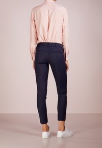 Camisa de manga larga de color rosa claro combinada con pantalones ajustados de color azul marino y zapatillas blancas. Los pantalones tienen una textura suave y bolsillos traseros.