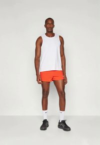 Valkoinen hihaton toppi, oranssit urheilushortsit, mustat lenkkarit ja valkoiset sukat. Asu on kevyt ja urheilullinen.