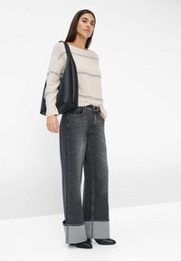 Chunky gebreid sweater in crème met grijze strepen, wijdvallende zwarte jeans met contrasterende lichte cuffs, en zwarte puntige schoenen. Zwarte tote bag.