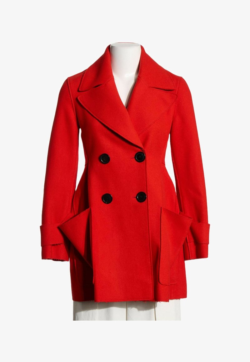 Manteau en laine rouge à double boutonnage avec larges revers, quatre boutons noirs, manches longues avec poignets et grandes poches avant en biais sur un mannequin blanc.