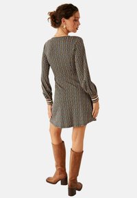 Vestido de manga larga en negro y beige con un patrón abstracto ondulado, cintura ceñida y puños acentuados. Se lleva con botas de tacón marrones hasta la rodilla.