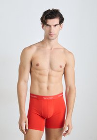 Piros pamut boxer alsónemű, testhezálló dizájnnal, széles Calvin Klein feliratos derékkal és sima textúrával.