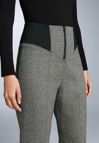 Texturált szürke halszálkás nadrág fekete elasztikus derékpanellel és elülső cipzárral. Testhezálló fazon, szabott kivitel.