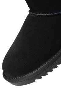 Bottine en daim noir avec semelle épaisse et texturée, et coutures visibles autour de l'orteil et du bord supérieur.