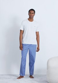 Hvit t-skjorte med korte ermer og subtil logo, kombinert med lyseblå bukser med rette ben. Glatt tekstur, ledig passform, minimalistisk design.