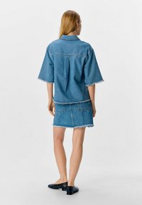 Tenue en denim composée d'une chemise à manches courtes ample avec des bords effilochés et d'une mini-jupe assortie à bords effilochés, le tout en bleu clair.