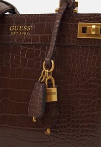 Bruine handtas met krokodillenstructuur en gouden hardware, voorzien van een logo-tag en een gestructureerd ontwerp. Textuur oppervlak met een elegante afwerking.