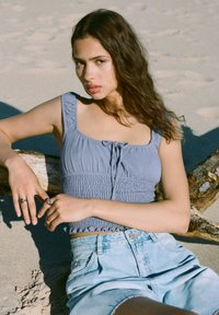 Svijetloplavi uski crop top s kvadratnim izrezom i detaljem snopa, uparen s trapericama visokog struka. Teksturalna tkanina, ležeran dizajn.