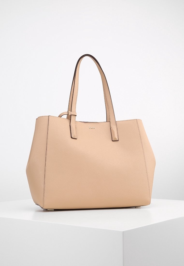 Sac fourre-tout en cuir beige avec doubles anses, forme rectangulaire et texture subtile, présenté sur un socle blanc.