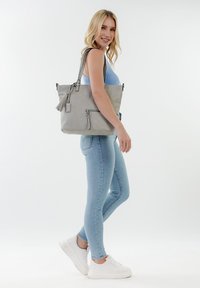Gray faux leather tote bag with a zippered pocket, tassel detail, and dual shoulder straps, featuring smooth texture and a rectangular shape.