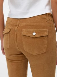 Spodnie z cordurowej tkaniny w ciepłym odcieniu brązu, z tylnymi kieszeniami z klapami i srebrnymi guzikami. Całość wykonana z teksturowanej, prążkowanej tkaniny.