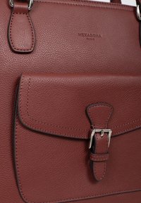 Borsa in pelle bordeaux con superficie texture, forma rettangolare, tasca frontale con pattina sicura tramite accessori in argento e logo in rilievo.