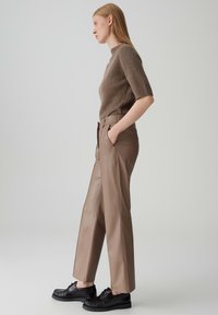 Beige geribde trui, hooggesneden bruine neplederen broek met wijde pijpen, en zwarte schoenen met textuuraccenten, gepresenteerd in een zijaanzicht.