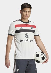 Hvit fotballdrakt med kort erm og rød og svart horisontale striper, med en logo og teksten "Snapdragon"; kombinert med grå shorts.